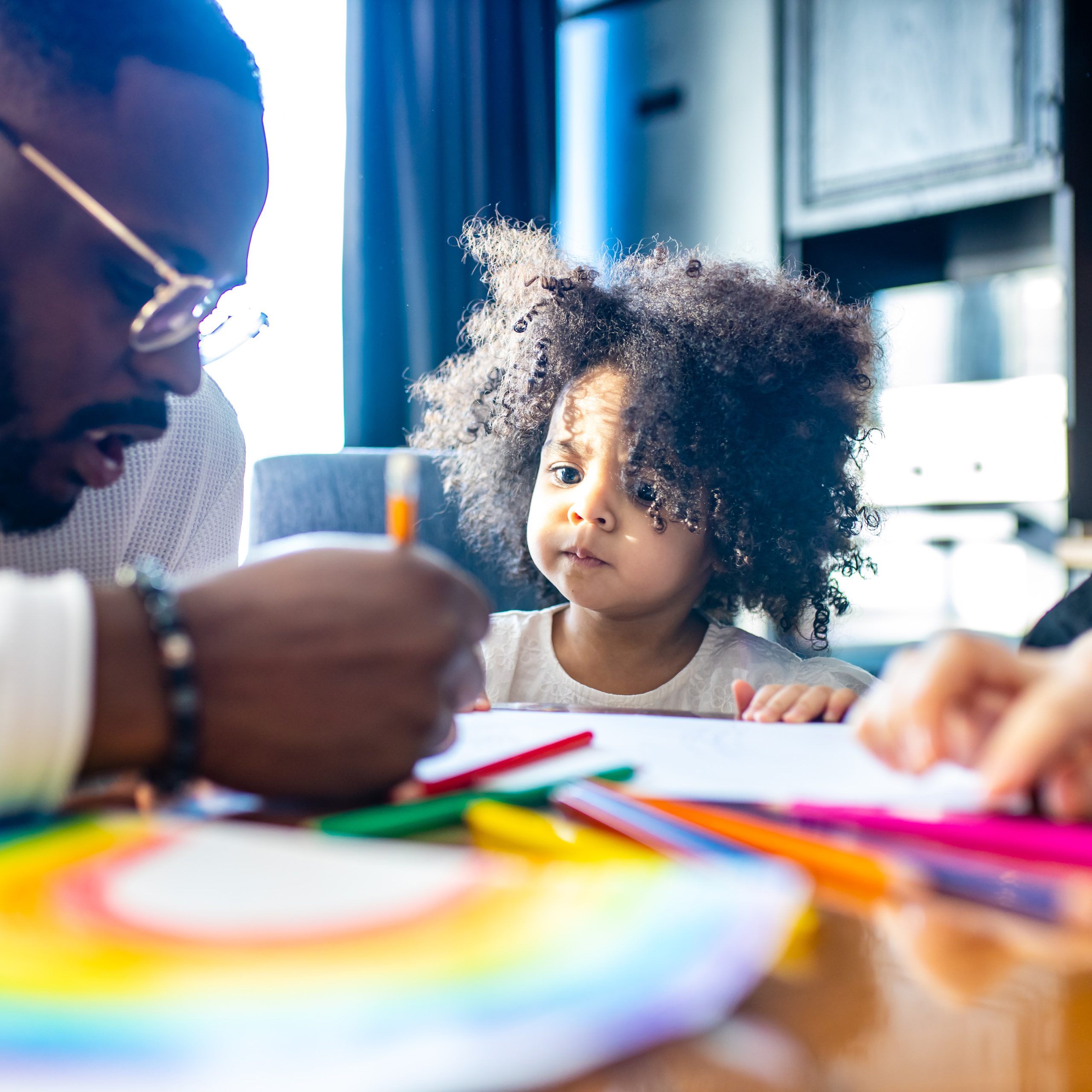 Man and small girl at table with markers and paper.
